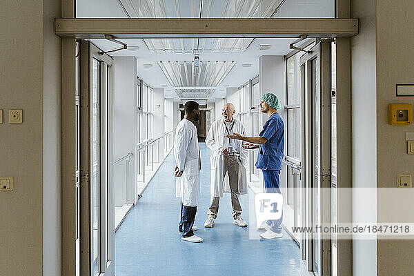 Full length of physician and doctors discussing while standing in corridor at hospital