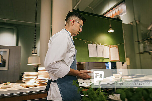 Seitenansicht eines männlichen Kochs  der Schüsseln hält  während er in einer Großküche geht