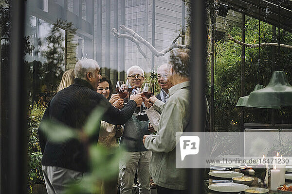Männliche und weibliche Freunde im Ruhestand stoßen mit Getränken auf einer Party an  gesehen durch Glas