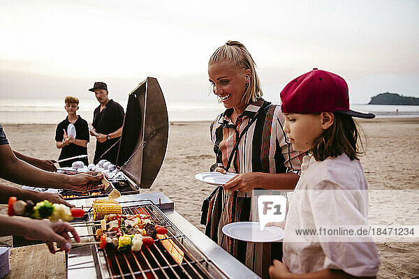 Mutter und Tochter stehen in der Nähe des Grills und halten Teller am Strand