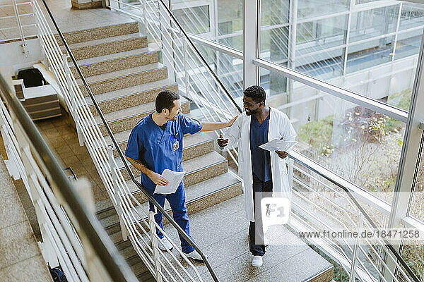 Hohe Winkel Ansicht der lächelnden männlichen Arzt und Krankenschwester diskutieren  während die Bewegung nach unten auf der Treppe im Krankenhaus