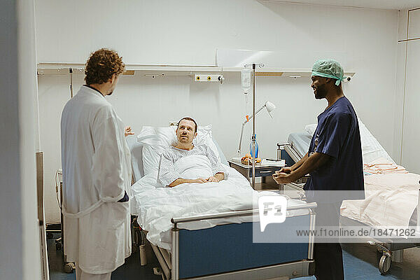 Männlicher Patient schaut den Arzt an  der neben der Krankenschwester im Krankenhaus steht