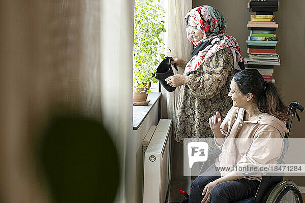Woman with paraplegia talking to mother watering plant at home