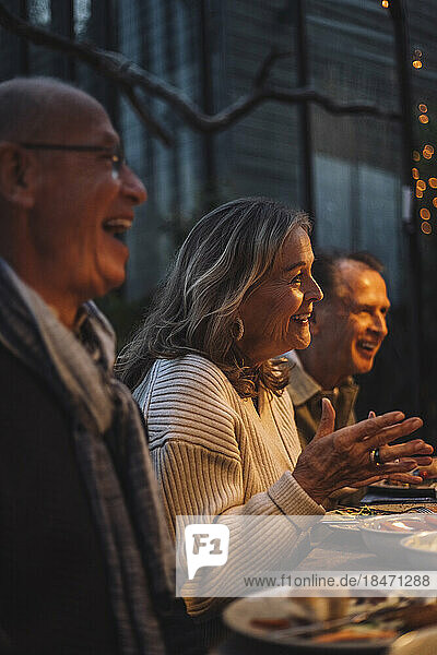 Glückliche ältere Frau gestikuliert beim Gespräch auf einer Dinnerparty