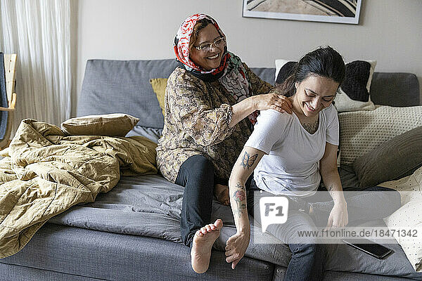 Glückliche Mutter massiert ihre querschnittsgelähmte Tochter  die zu Hause auf dem Sofa sitzt