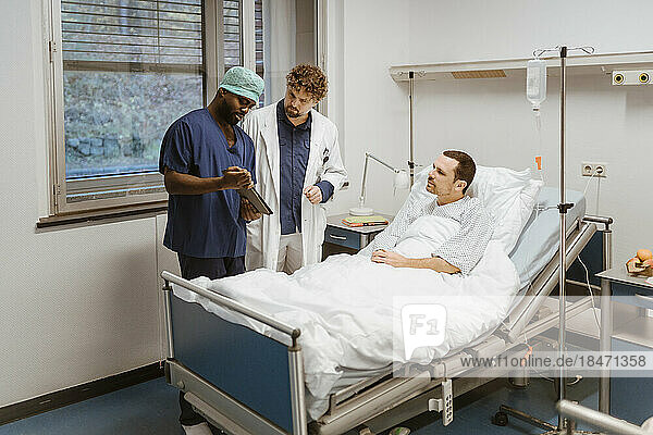Ein Krankenpfleger zeigt einem Arzt und einem Patienten im Krankenhaus ein digitales Tablet