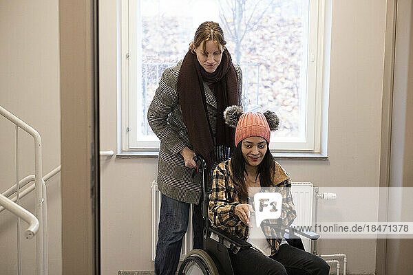 Weibliche Pflegekraft hilft einer Frau  die zu Hause im Rollstuhl sitzt