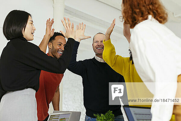 Happy multiracial colleagues giving high-five in office