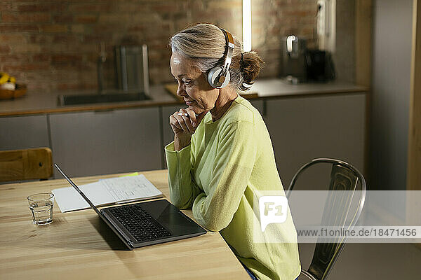 Freelancer wearing wireless headphones using laptop at desk