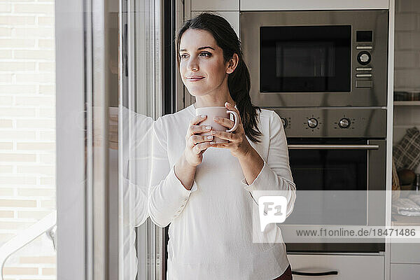 Thoughtful woman with coffee cup standing near window