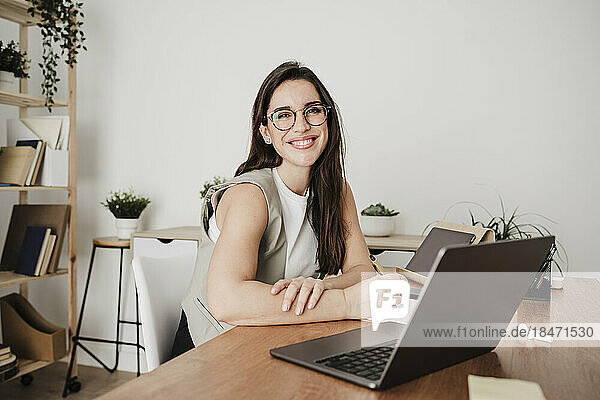Happy businesswoman sitting in front of laptop at office desk