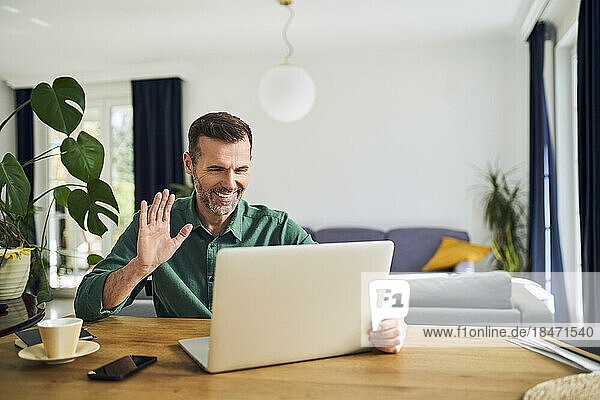 Cheerful man making video call waving at laptop