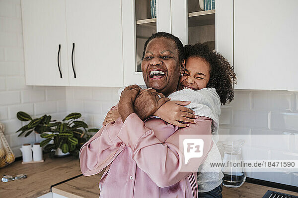 Cheerful girl embracing grandmother in kitchen at home