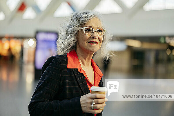 Mature businesswoman wearing eyeglasses with disposable coffee cup at subway station