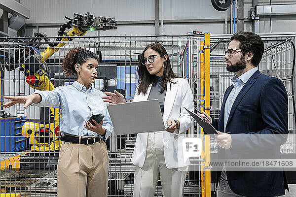 Businesswoman holding laptop discussing with colleagues in factory