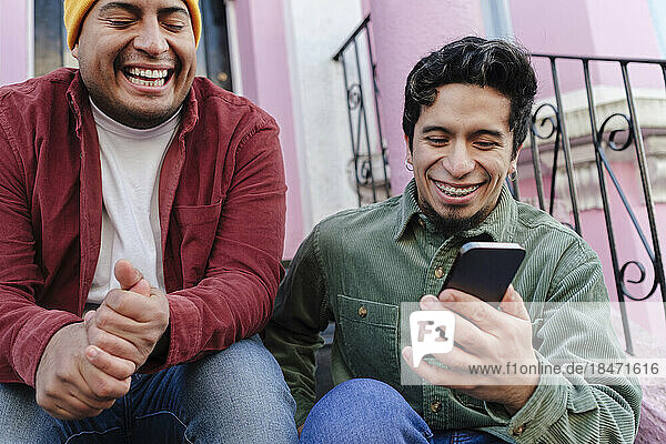 Cheerful man with brother using mobile phone