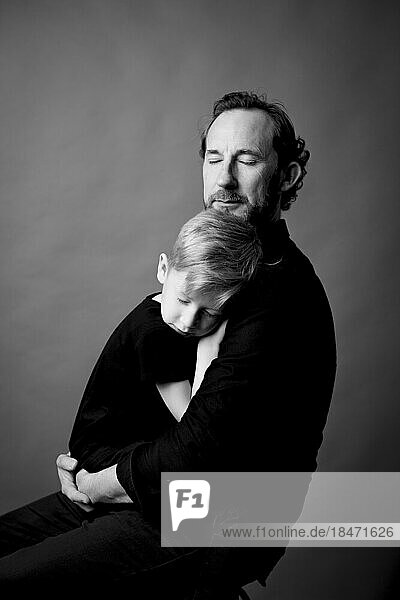 Zärtlicher Vater mit geschlossenen Augen umarmt seinen Sohn