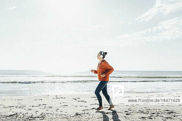 Reife Frau mit Kopfhörern joggt am Strand