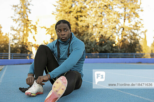 Thoughtful athlete tying shoelace sitting on sports track