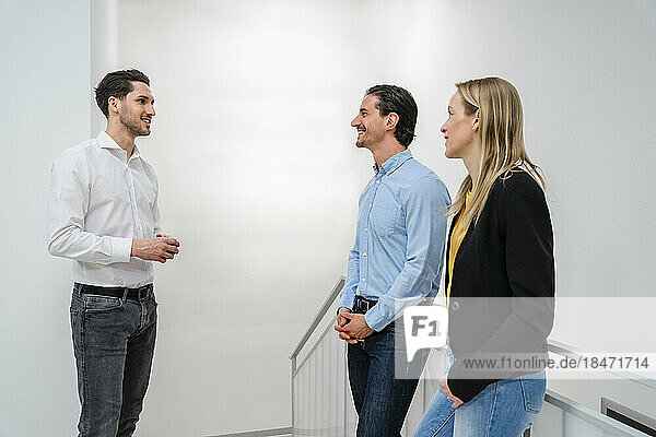 Smiling businessman talking to colleagues standing near railing at office