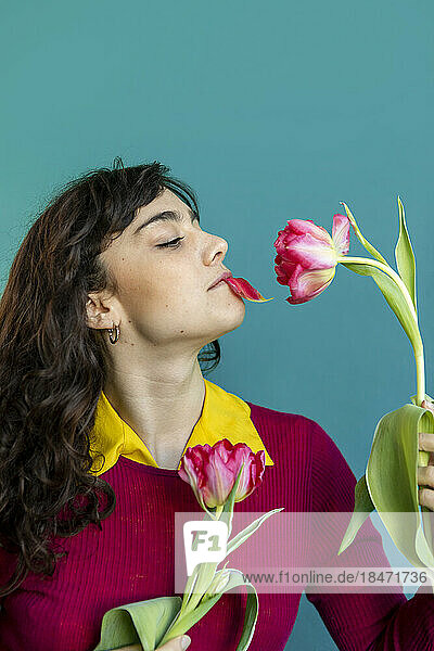 Woman with tulip petal in mouth against green background