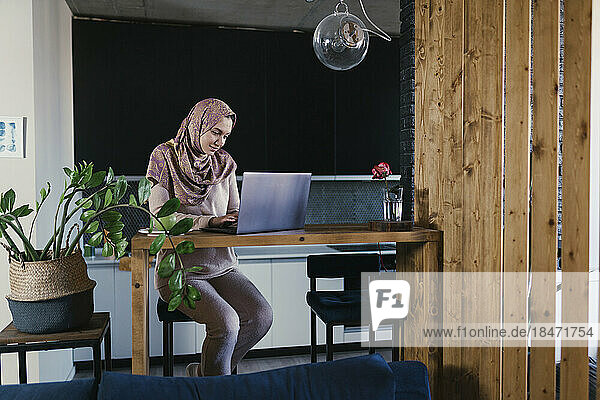 Freelancer wearing hijab working on laptop at home office