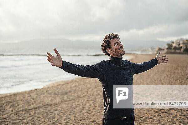 Carefree man with arms outstretched standing in front of sea