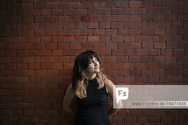 Thoughtful young woman with bangs standing in front of brick wall