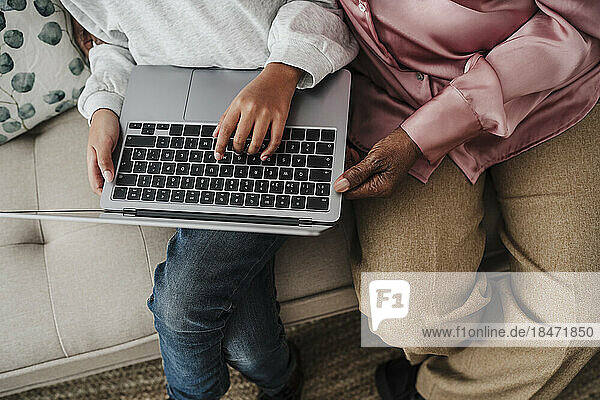 Mädchen benutzt Laptop und Großmutter sitzt zu Hause auf dem Sofa