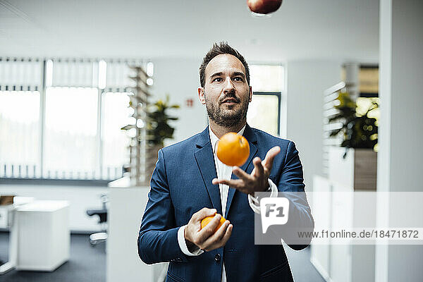Geschäftsmann jongliert mit Orangenfrüchten im Büro