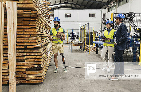 Engineer examining stack of planks with colleagues in factory