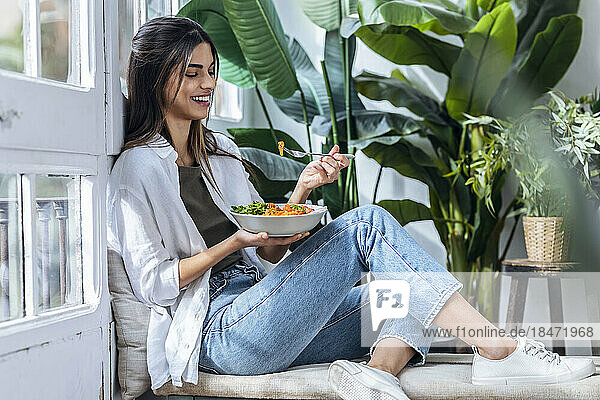 Happy woman eating salad at the window