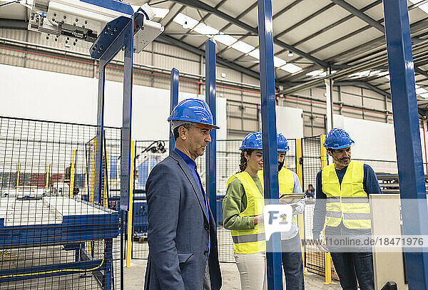 Engineer wearing hardhat with colleagues in factory