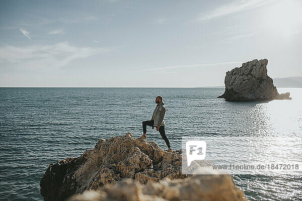 Mann steht bei Sonnenuntergang auf einem Felsen vor dem Meer