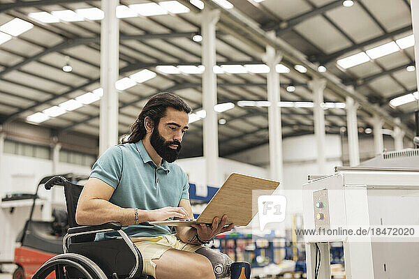 Engineer sitting in wheelchair working on laptop in robotics factory