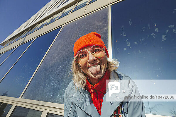 Playful woman sticking out tongue near building
