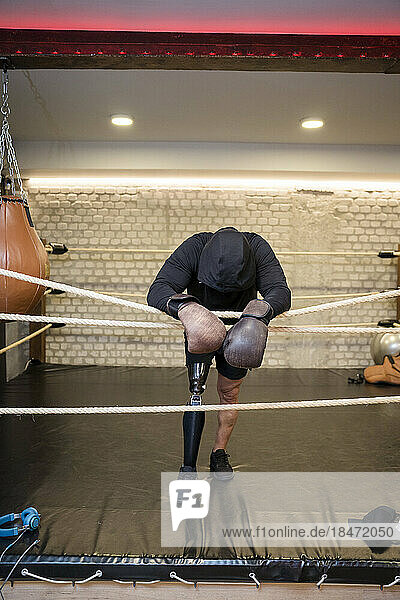Mature man with prosthetic leg leaning on rope in boxing ring