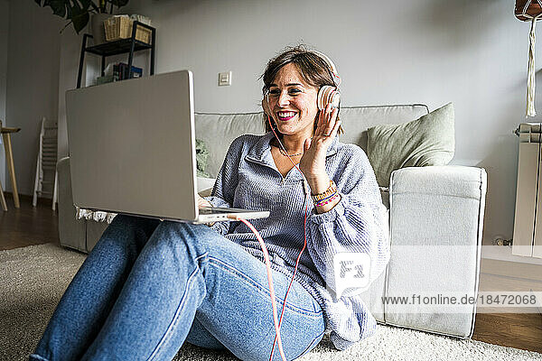 Happy woman waving through laptop sitting on floor at home