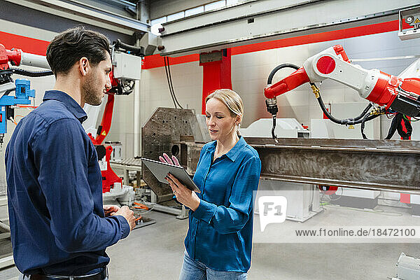 Mature technician holding tablet PC discussing with engineer in robot factory