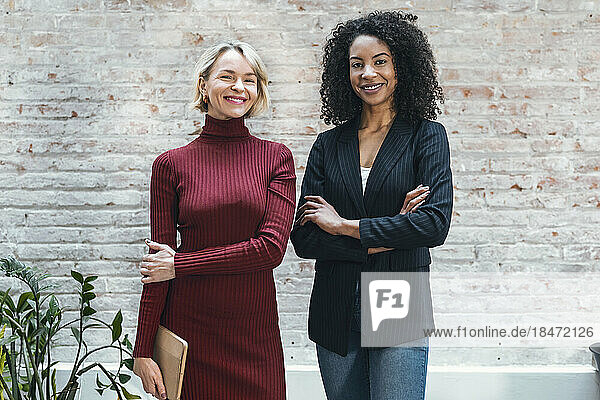 Happy businesswoman standing with colleague in front of wall