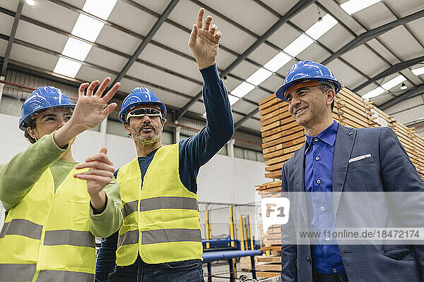 Engineer with colleague wearing smart glasses gesturing at transparent screen in factory