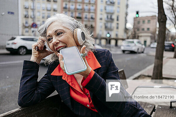 Happy businesswoman talking on speaker phone in city