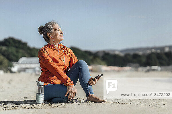 Smiling woman listening to music through in-ear headphones at beach