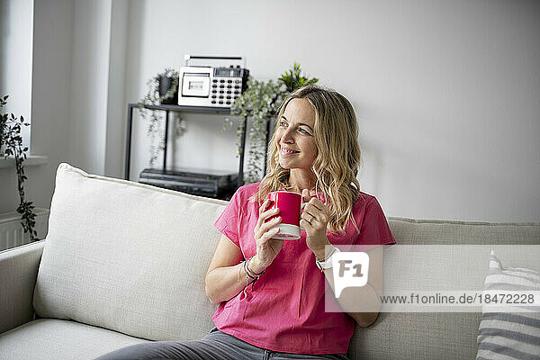 Smiling mature woman holding coffee cup sitting on sofa at home