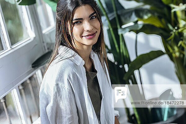 Smiling young woman in front of plants at the window