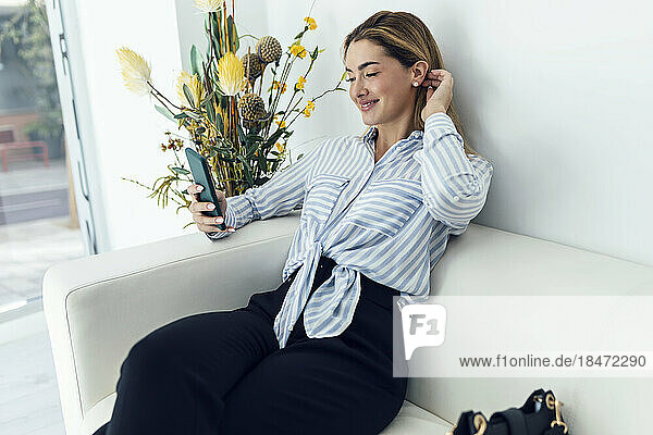Lächelnde Frau  die auf dem Sofa sitzt und ihr Smartphone benutzt