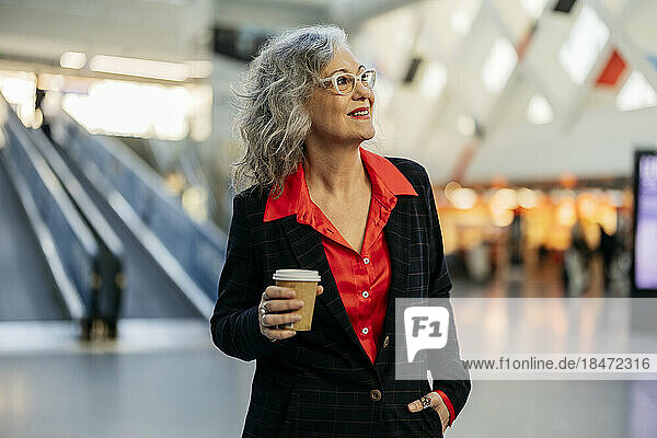 Happy mature businesswoman with disposable coffee cup at subway station