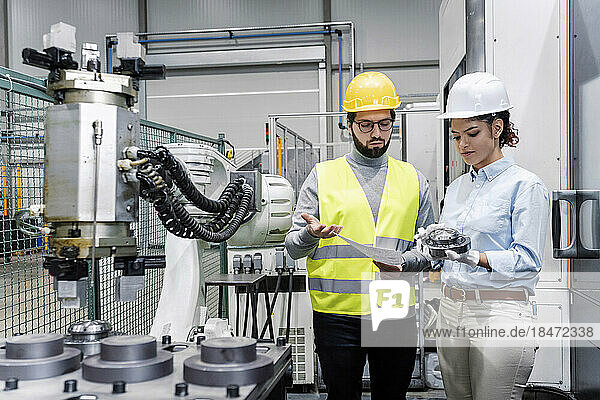 Businesswoman showing machine part to engineer in factory