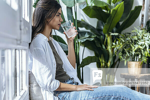 Young woman drinking water sitting by plants