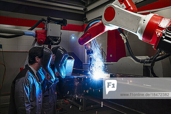 Engineers near robotic arm doing welding in industry